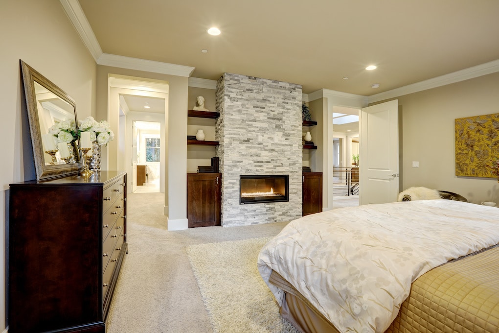 Beige and brown master bedroom boasts queen bed facing gorgeous stone fireplace framed by shelves.