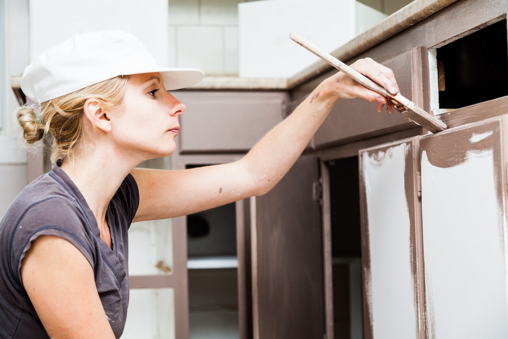 Woman painting after choosing between refacing vs. replacing kitchen cabinets
